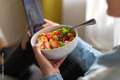 Close up of a Smiling young woman sitting on a chair and taking a selfie with her salad in her room