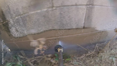 Power washing the dirty brick wall at backyard with high pressure washer, POV photo