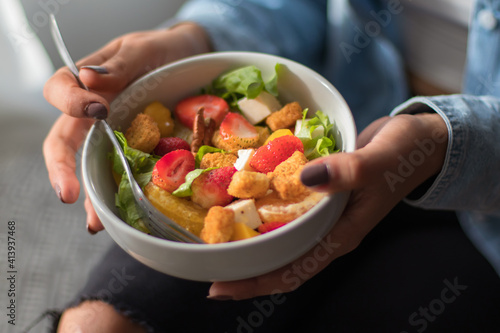 Close up of a  woman eating a salad. She is sitting on a sofa in her room