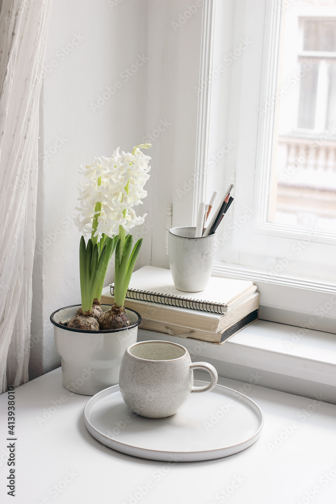 Easter spring still life. Cup of coffee, book and blank diary near window sill. White hyacinth in flower pot. Pencils in ceramic holder. Home office concept. Scandinavian interior. Vertical.