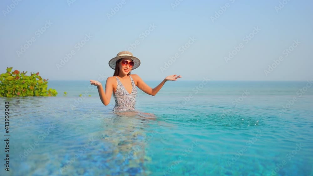 Asian woman with big sunglasses and hat plays with water in infinity pool. Slow-motion Asian woman with big sunglasses and hat plays with water in infinity pool. Slow-motion