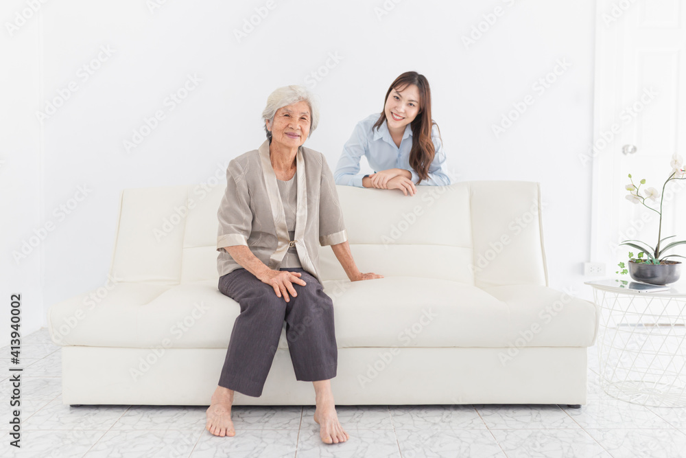Obraz premium young Asian female hug old female in home, they feeling happy and smile, they sitting on sofa, mother's day, happiness elderly in family time