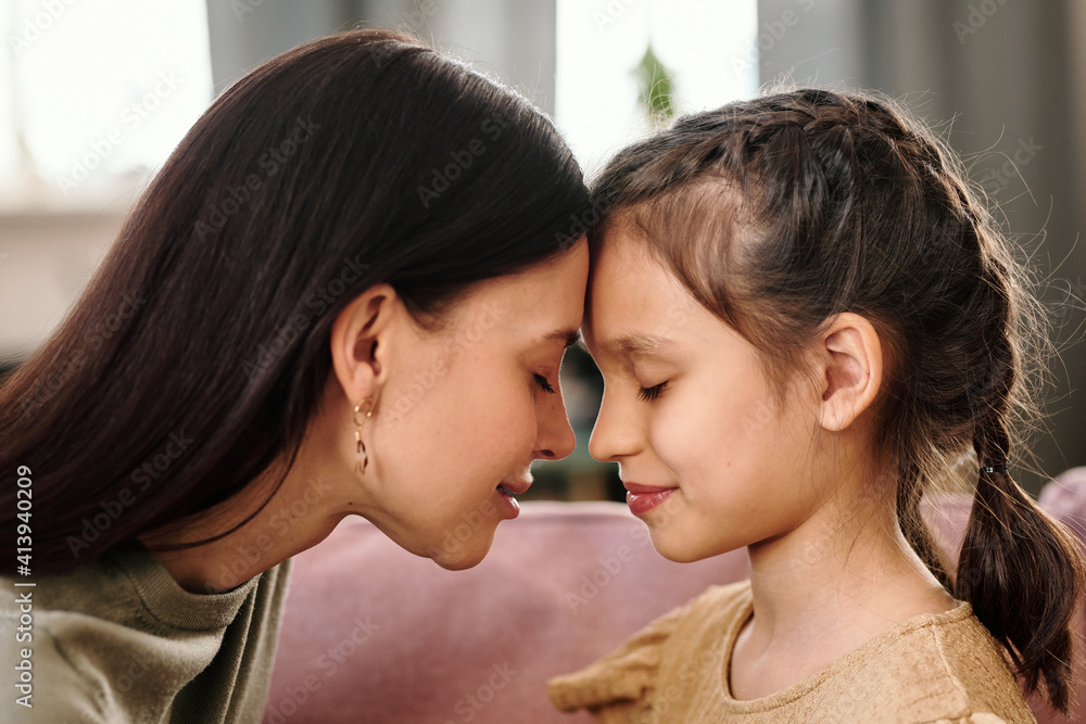 Side view of young brunette woman and her little daughter touching by foreheads