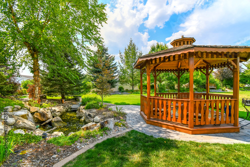 A nicely landscaped garden and back yard with a round wooden cedar gazebo and a pond with waterfall photo