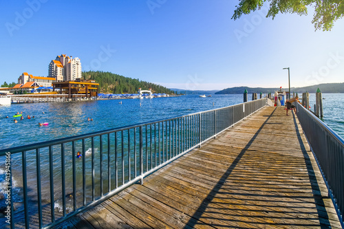 A young boy leans over the dock edge at afternoon at a lakefront wooden dock with a hotel resort and mountain behind in Coeur d'Alene Idaho USA 