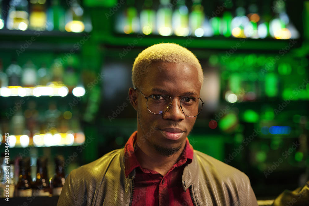 Young African man in smart casualwear and eyeglasses standing against bar Young African man in smart casualwear and eyeglasses standing against bar