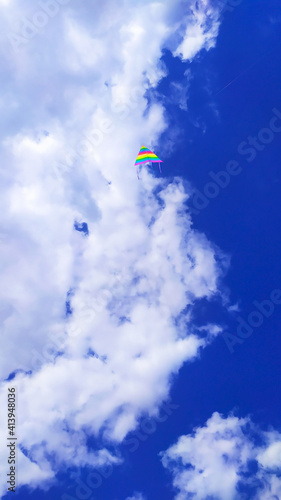 vertical photo of a blue sky half-covered with snow-white clouds, including a multi-colored airplane