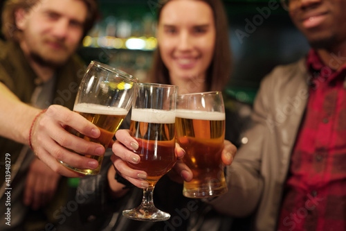 Hands of happy young intercultural football fans clinking with glasses of beer