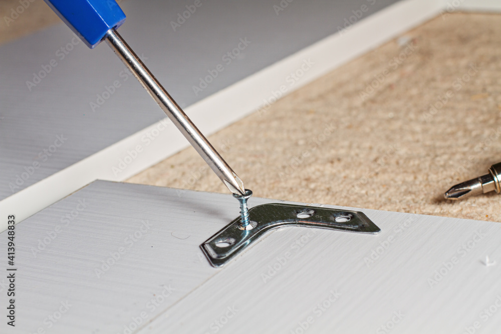 Obraz premium The screwdriver twists the screw into a brown wooden board in the corner, horizontal photo