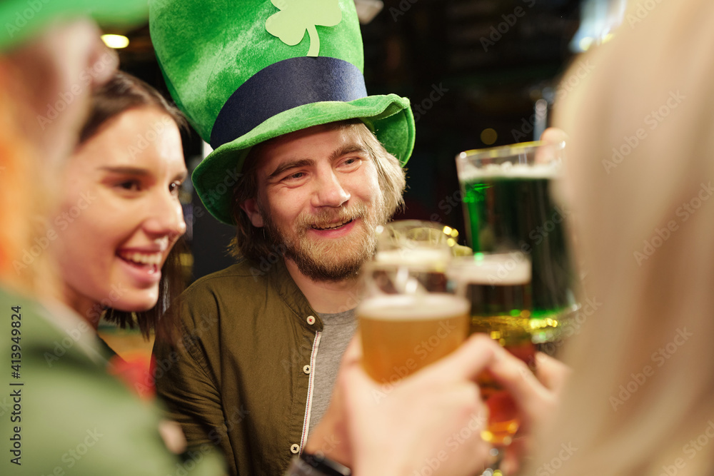 Happy young bearded man in traditional green irish hat toasting with his friends Happy young bearded man in traditional green irish hat toasting with his friends