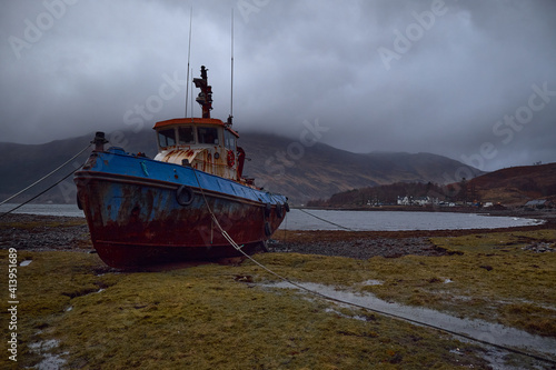 Abandoned fishing boat stranded ashore in the Scottish Highlands, Uk. Abandoned, rusty and dilapidated. Stormy day with many clouds and fog in the environment.