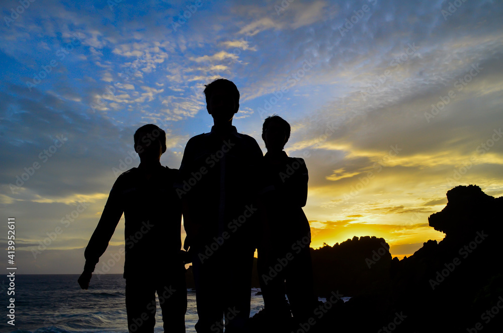 silhouette of group of friends standing in sunset at beach