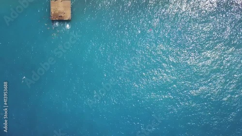 Aerial top view of a blue sea and wooden pier. Clip. Sandy beach with people sunbathing outdoors, concept of summer vacation. photo