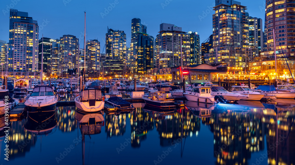 Night exposure of downtown Vancouver, British Columbia, Canada. One of the most vibrant cities in North America. Blue clear sky with water reflections lights trail, stars, and glitters.
