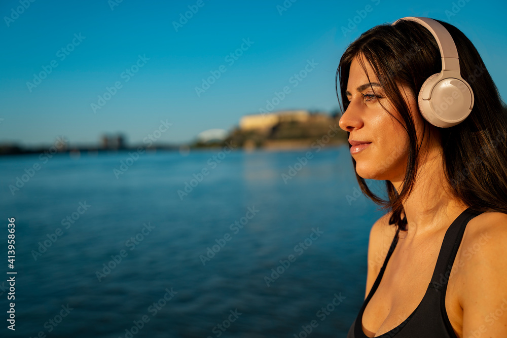 Beautiful young woman with headphones by the sea, wearing tank top, closeup shot