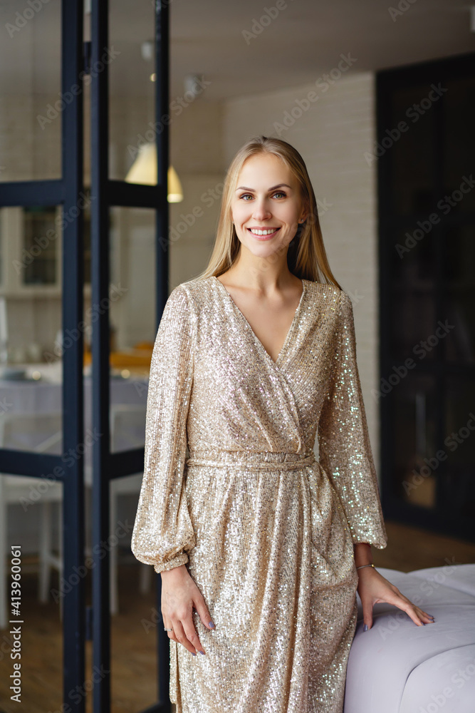 Pretty young woman portrait indoors. Blonde sexy young beautiful woman in golden dress with sequins in a room. Home party or preparation for a date. Luxurious dress. Modern living room Pretty young woman portrait indoors. Blonde sexy young beautiful woman in golden dress with sequins in a room. Home party or preparation for a date. Luxurious dress. Modern living room