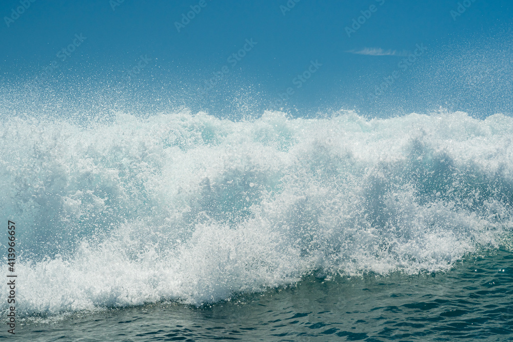 White foamy water on a tropical turquoise breaking ocean wave with blue sky background.