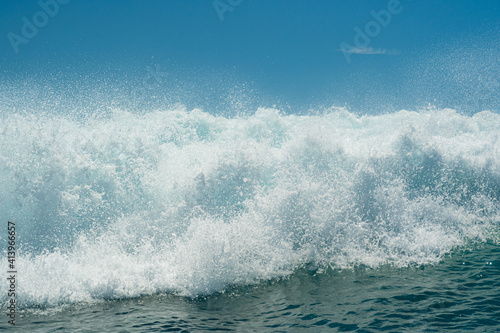 White foamy water on a tropical turquoise breaking ocean wave with blue sky background.