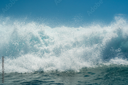 White foamy water on a tropical turquoise breaking ocean wave with blue sky background.