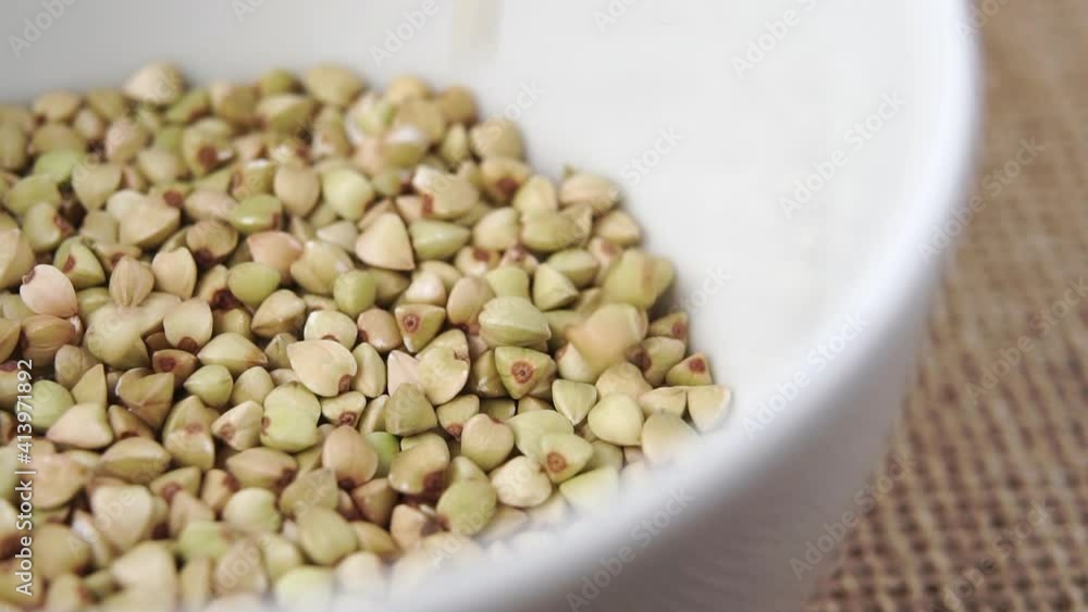 Macro shot falling green buckwheat seeds in a heap in a white bowl. Slow motion Macro shot falling green buckwheat seeds in a heap in a white bowl. Slow motion