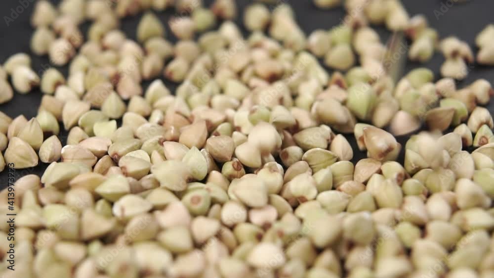 Bio product green buckwheat is poured in slow motion on a dark stone surface. Macro shot Bio product green buckwheat is poured in slow motion on a dark stone surface. Macro shot