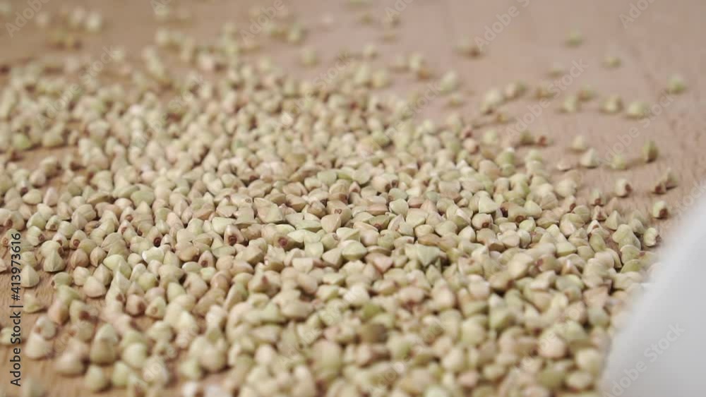 Scattering uncooked green buckwheat from a white bowl onto a wooden surface in slow motion. Close-up. Bio healthy food Scattering uncooked green buckwheat from a white bowl onto a wooden surface in slow motion. Close-up. Bio healthy food