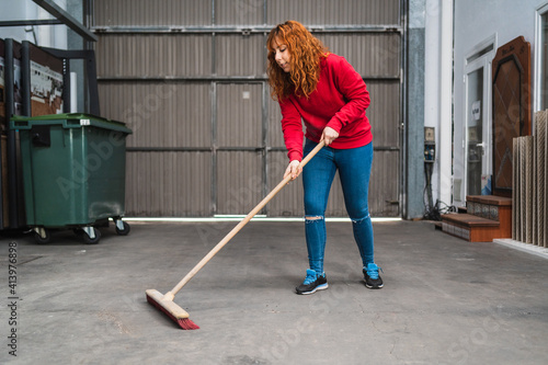 Female worker sweeping the garage with a large broom