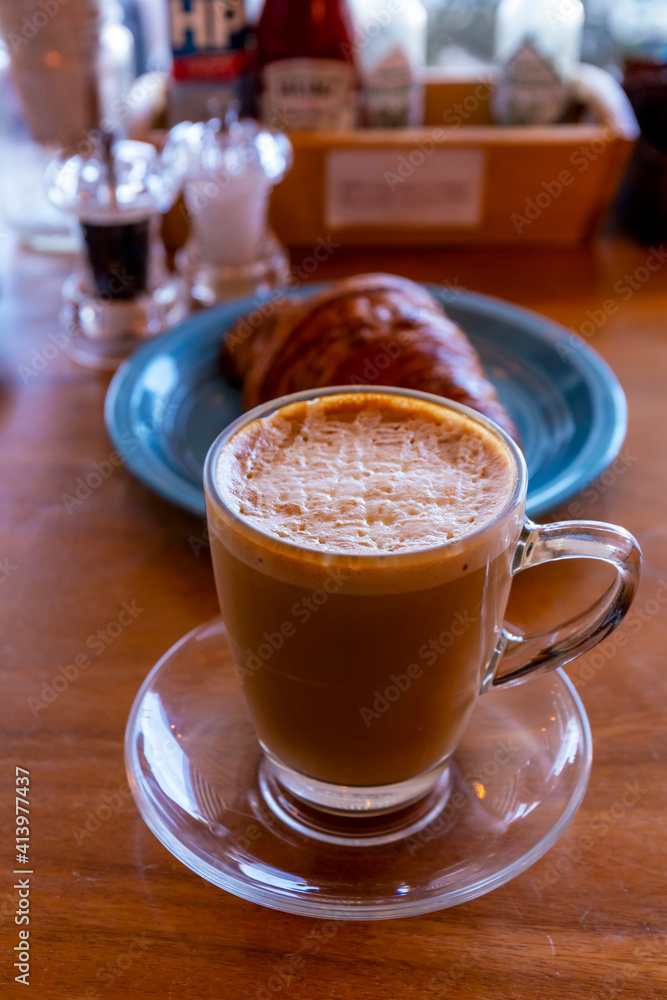 Close up hot cappuccino, latte on table with blur coffee shop background. Hot cappuccino coffee on wood table with blur croissant background. breakfast at coffee shop. softfocus select coffee Close up hot cappuccino, latte on table with blur coffee shop background. Hot cappuccino coffee on wood table with blur croissant background. breakfast at coffee shop. softfocus select coffee