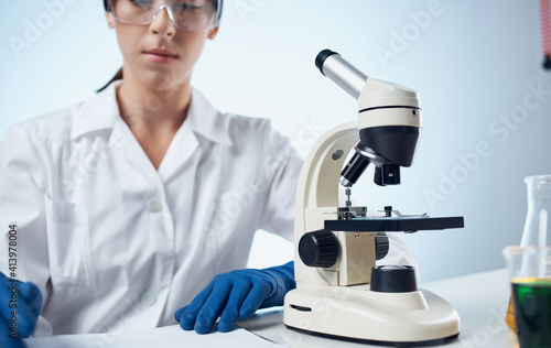 female laboratory assistant examines bacteria through a microscope and glasses on the face chemical element vaccination