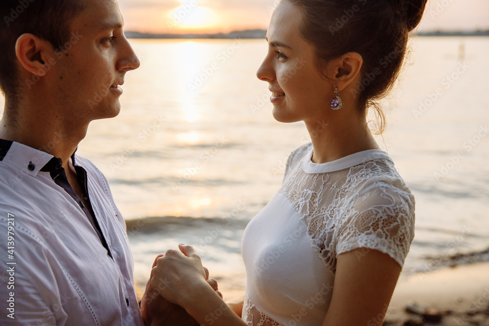 Fototapeta premium Beautiful enamored man and woman take an oath of love on the river bank. Young people hold each others hands. The eyes of young people are directed at each other. High quality photo