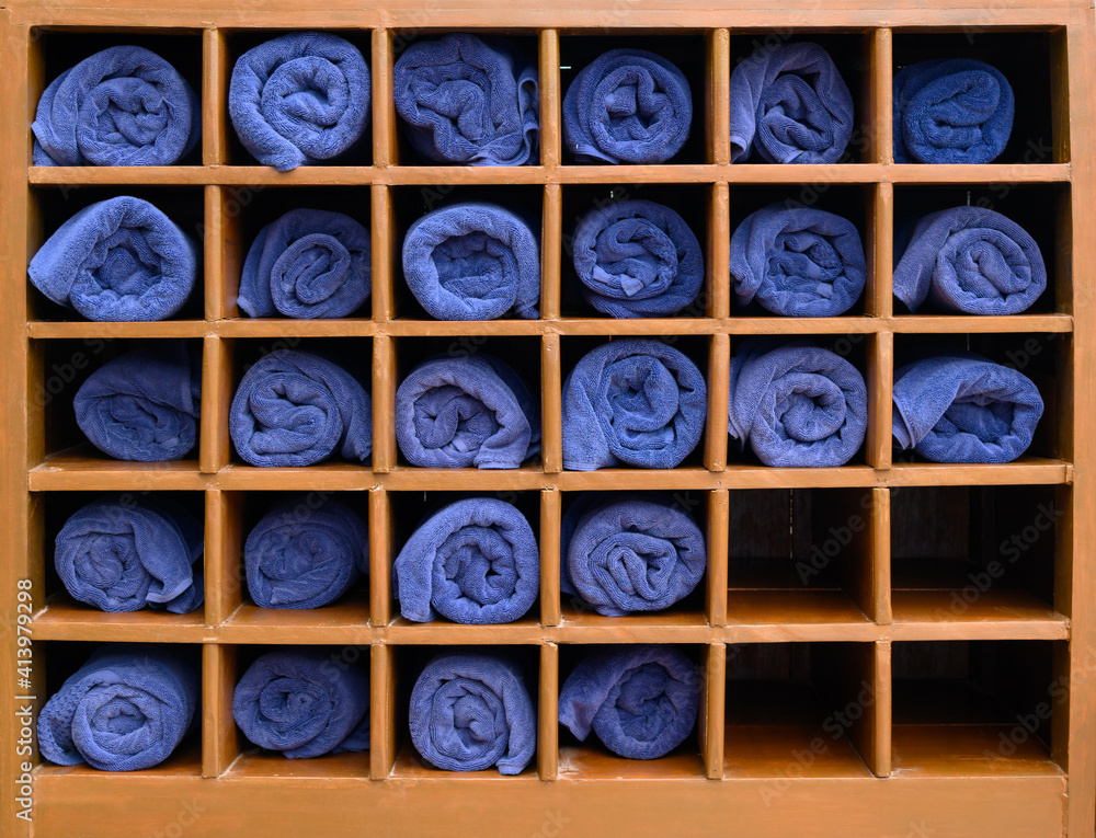 Rolled blue bath towels in wooden box shelf for travellers at swimming pool, sea beach, gym fitness in resort hotel concept.