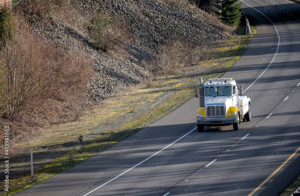 Big rig utility towing semi truck running on the turning road to emergency call point for help.