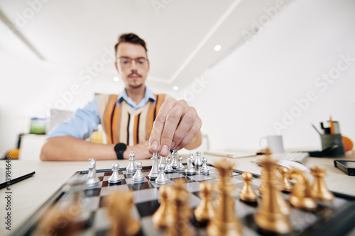 Intelligent young university student moving queen piece when playing chess, selective focus