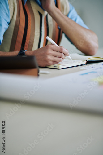 Close-up image of businessman writing down his thoughts on how to make his work more efficient in planner