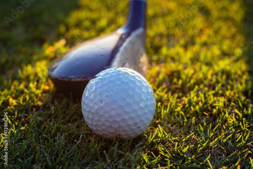close-up of golf ball and club on green with sunset light