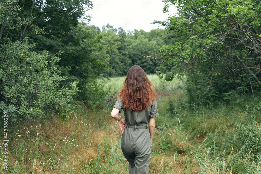 brunette woman in overalls on the meadow back view
