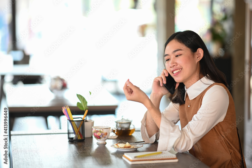 Cheerful young woman talking on mobile phone while siting in modern coffee shop. Cheerful young woman talking on mobile phone while siting in modern coffee shop.