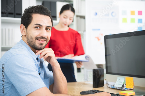 Young asian man working on a computer at workplace. He looked straight at the camera and smile