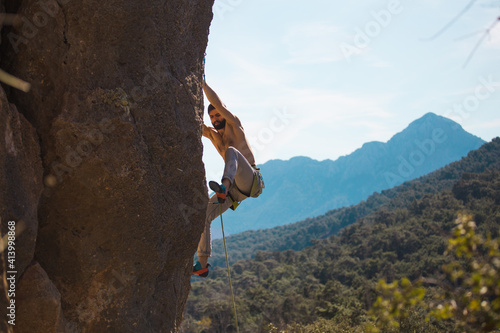 A rock climber climbs a rock against the background of mountains and sky