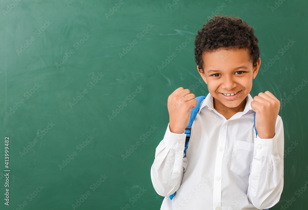 Happy little African-American schoolboy near chalkboard in classroom