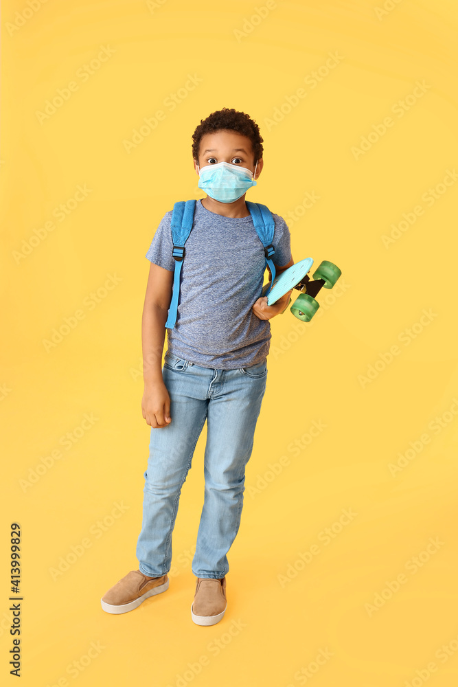 Fototapeta premium Little African-American schoolboy in medical mask and with skateboard on color background. Coronavirus epidemic