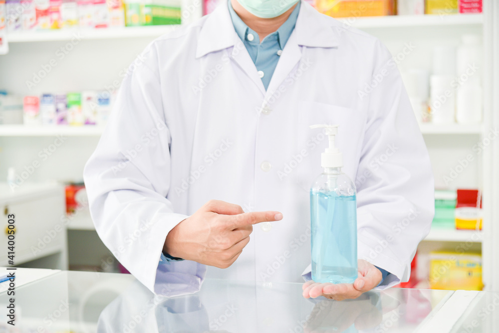 Pharmacist holding alcohol gel bottle and pointing to it at drugstore. Pharmacist holding alcohol gel bottle and pointing to it at drugstore.