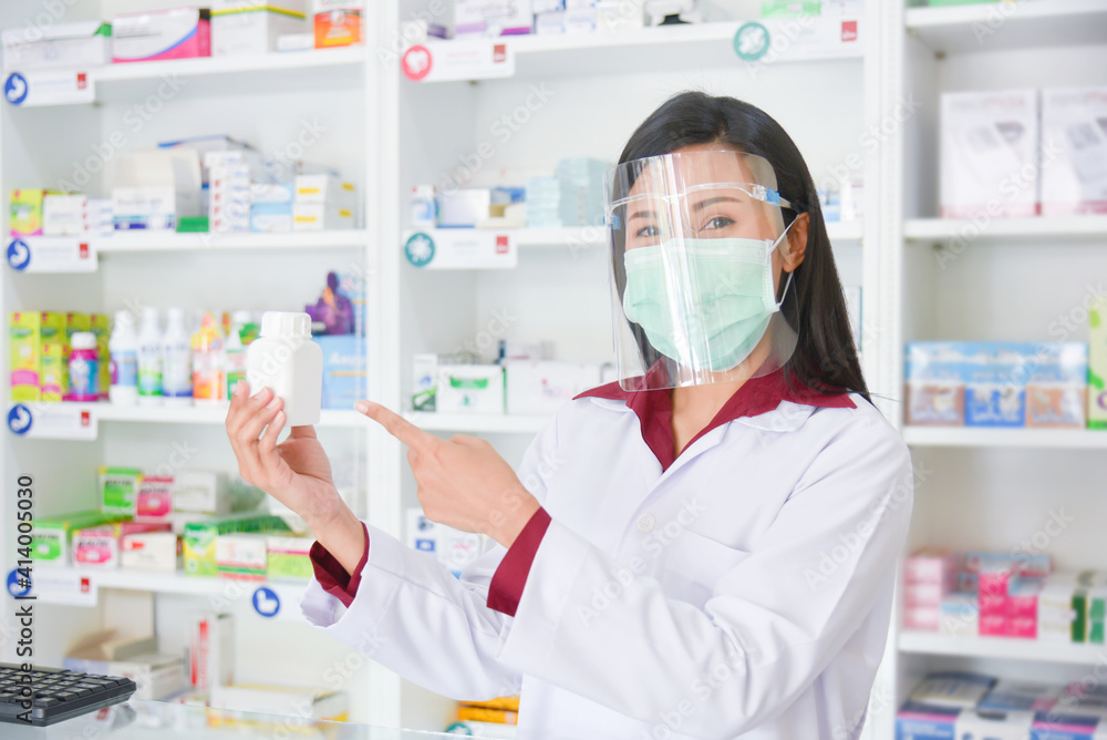 Asian professional young pharmacist wearing faceshield and mask while medication explain at drugstore.