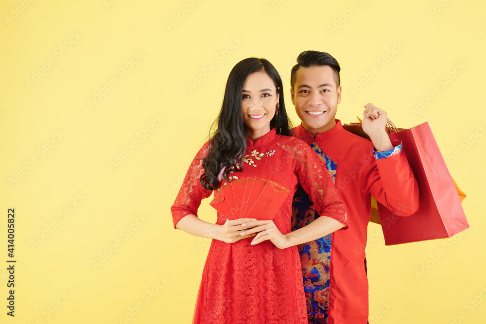 Cheerful young Asian couple with lucky money envelopes and shopping bags ready for Chinese New Year celebration Cheerful young Asian couple with lucky money envelopes and shopping bags ready for Chinese New Year celebration