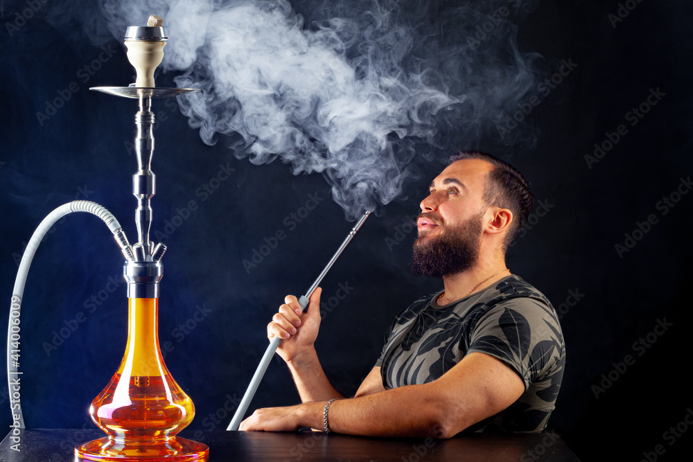 Bearded young man smoking shisha in a dark night club