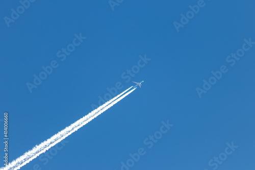 Flying airplane on a journey through the blue sky with a long white smoking exhaust plume and jetwash shows international transportation and globalization transatlantic holidays with pilots