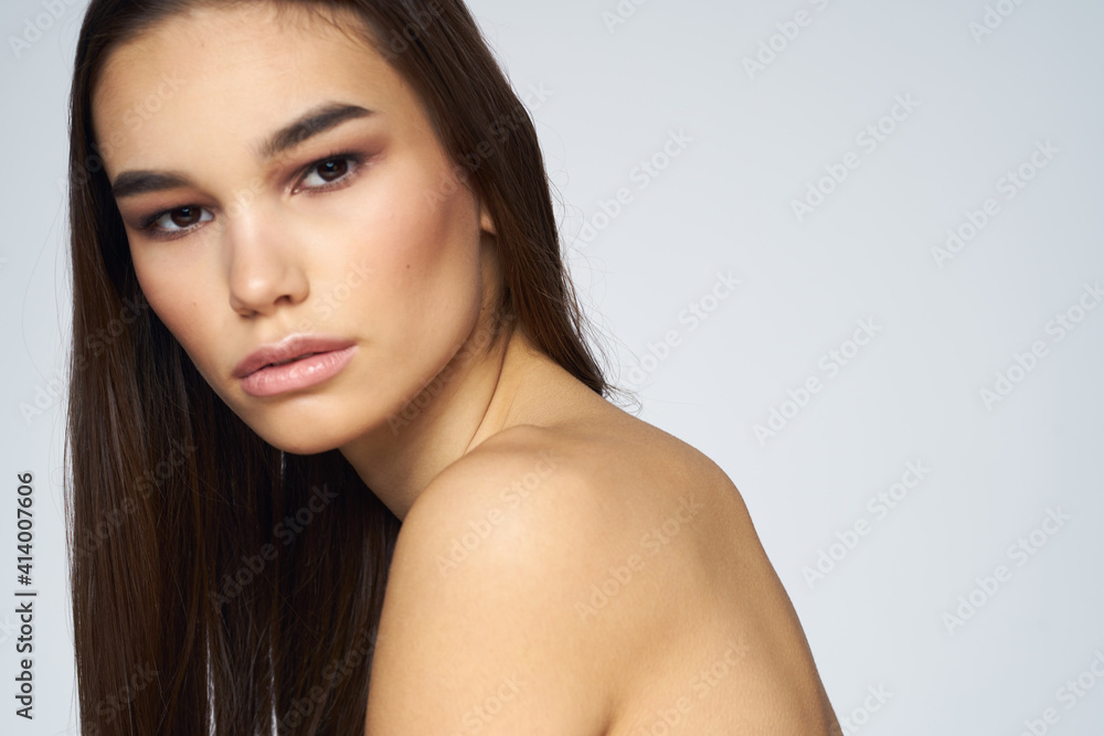 Pretty brunette naked shoulders long hair close-up light background Pretty brunette naked shoulders long hair close-up light background