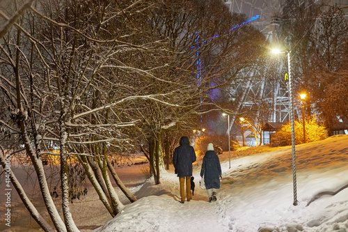 Couple on Alley in cold winter park with snow at night and and the lights in the background