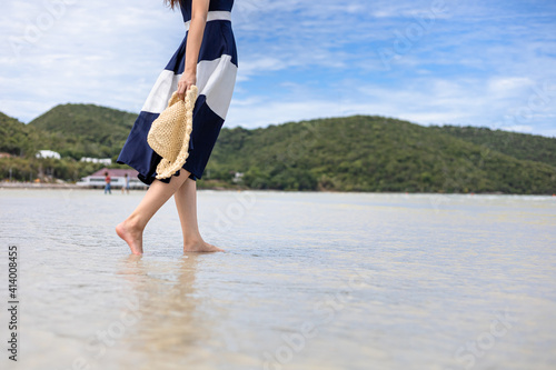 Woman barefoot hold hat and walking on summer along wave of sea water and sand on the beach.
