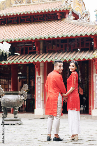 Happy young Asian couple in traditional dresses walking to Buddhism temple, turning back and smiling at camera © DragonImages